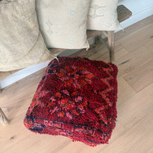 Load image into Gallery viewer, Red and black patterned throw blanket on a wooden floor with beige pillows in the background.