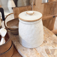 Load image into Gallery viewer, White ceramic jar with a wooden lid on a marble surface in a rustic setting.
